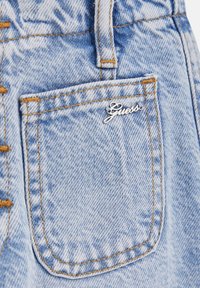 Ljust blå denimshorts har en framficka med en silverfärgad "Guess"-logotyp, kontrasterande orange sömmar och en texturerad tygfinish.
