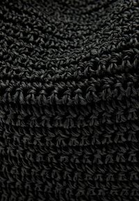 Czarny dzianinowy tekstyl z fakturowanym wzorem splotu. Materiał wydaje się wytrzymały i gruby, z równomiernie rozmieszczonymi oczkami.