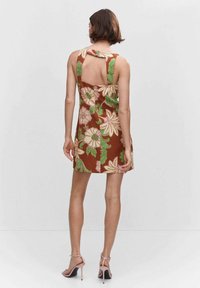 Robe florale marron avec motifs verts et roses, sans manches, découpe au dos et détail noué à l'épaule. Assortie à des talons roses.