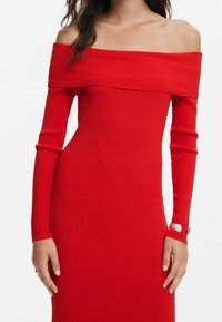 Robe rouge côtelée à épaules dénudées avec manches longues ; présente une coupe ajustée et des accents de boutons argentés aux poignets des manches.