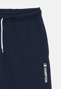 Mørkeblå joggebukser laget av en bomullsblanding. Har en hvit snor og en trykket Champion-logo på venstre ben. Glatt tekstur.