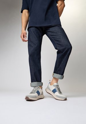Jeans en denim bleu foncé avec des ourlets retroussés, associés à des baskets grises et blanches avec des accents bleus et des panneaux texturés.