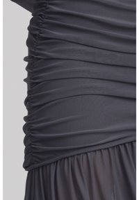 Robe gris foncé avec texture froncée sur le corsage et jupe transparente fluide. Tissu léger avec une finition lisse et détails de rassemblement élastiques.