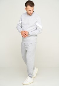 Grauer Hoodie und passende Jogginghose aus weichem Material. Der Hoodie hat weiße Akzente an den Ärmeln. Helle Sneakers runden das Outfit ab.