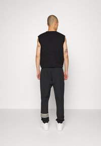 Czarny bezrękawnik, luźne czarne spodnie z białym paskiem na mankietach i białe trampki. Materiał wydaje się gładki; całość w swobodnym fasonie.