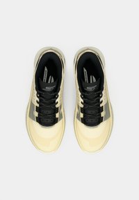 Ζευγάρι μπεζ και μαύρα αθλητικά παπούτσια μπάσκετ, φωτογραφημένα από ψηλά σε λευκό φόντο, με ορατά τα κορδόνια και τις εσωτερικές σόλες.