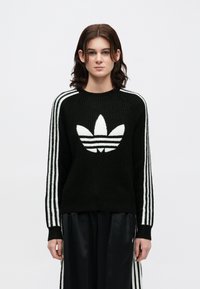 Suéter preto de malha com detalhes brancos em três riscas nas mangas e um grande logótipo branco centrado no peito. Gola redonda clássica.