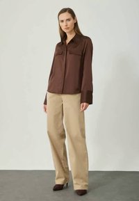 Brown satin shirt with two chest pockets, paired with beige wide-leg trousers. The outfit is complemented by dark heels.