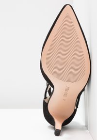 Semelle d'une chaussure à talon haut noire à bout pointu avec lignes de grip texturées et taille 37 imprimée sous la voûte plantaire.