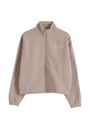 Sweat-shirt beige zippé avec col montant, manches longues avec poignets élastiqués, et petit texte blanc sur la partie gauche de la poitrine.