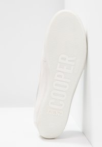 Bílé tenisky s hladkým koženým svrškem a texturovanou gumovou podrážkou. Na podrážce je vytlačený nápis "COOPER" a kruhový vzor pro lepší přilnavost.