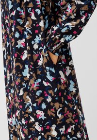 Blumendruckkleid in Marineblau mit bunten Mustern in Pink, Blau und Weiß. Mit gerafften Ärmeln und seitlichen Taschen. Glatte Stofftextur.
