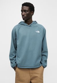 Φούτερ με κουκούλα από ανοιχτό μπλε φλις, με τσέπη καγκουρό, κουκούλα με κορδόνια και λευκό λογότυπο στο στήθος, σχεδιασμένο με άνετη γραμμή.