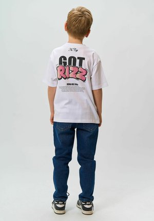 Witte katoenen t-shirt met "GOT RIZZ" in vette roze en zwarte letters op de achterkant, gecombineerd met blauwe jeans en zwart-witte sneakers.