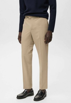Pantalones beige de corte recto, con bolsillos laterales y cierre de un solo botón. Combinados con mocasines negros.