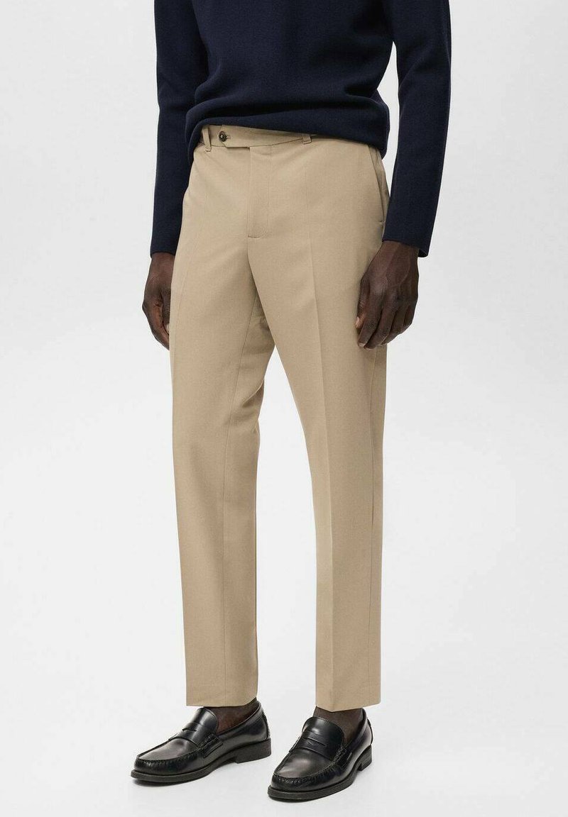 Pantalones beige de corte recto, con bolsillos laterales y cierre de un solo botón. Combinados con mocasines negros.