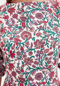 Kurzärmlige Bluse mit floralem Muster in lebendigen Farbtönen von Pink, Rot und Grün auf weißem Hintergrund, aus leichtem Stoff gefertigt.