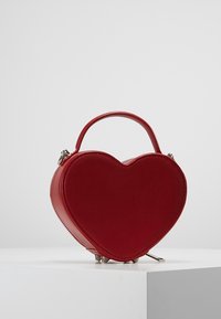 Rode handtas in de vorm van een hart, gemaakt van glad leer, met een bovenhandvat, zilveren hardware en een ritssluiting. Verfraaid met kleine metalen voetjes.