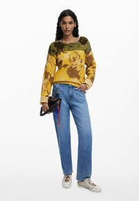 Gelb-braun gestreifter Strickpullover mit Rundhalsausschnitt, kombiniert mit hellblauen geraden Jeans und einer schwarzen Handtasche.