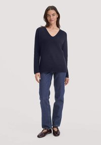 Marineblauer Strickpullover mit V-Ausschnitt, kombiniert mit gerade geschnittenen blauen Jeans und dunkelbraunen Schuhen. Weiche Textur und entspannte Passform.