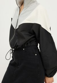 Zwart-grijs jack met ritssluiting, hoge kraag, elastische zoom en lange mouwen; met contrasterend colorblock-ontwerp en trekkoorddetail.