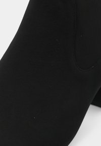 Černá kotníková obuv z měkkého, strukturovaného materiálu s elegantním siluetem a bez viditelných kovových částí nebo akcentů. Hladký povrch s jemným leskem.