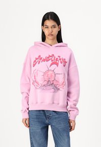 Túlnagy rózsaszín kapucnis pulóver grafikus mintával, amelyen nap és hegy látható, zsinóros kapucni, és bordás mandzsetták. Kényelmes fleece anyag.