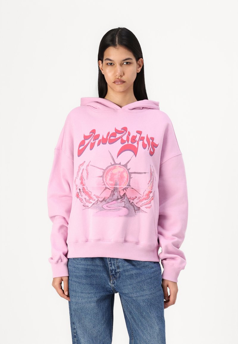 Túlnagy rózsaszín kapucnis pulóver grafikus mintával, amelyen nap és hegy látható, zsinóros kapucni, és bordás mandzsetták. Kényelmes fleece anyag.