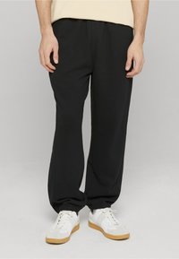 Zwarte sweatpants met elastische boorden, gemaakt van zachte stof, gecombineerd met witte en beige sneakers. Vooraanzicht, geen zichtbare patronen.