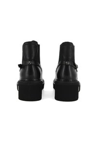 Botas de cuero negro hasta el tobillo con una suela gruesa, punta redondeada y correas ajustables. Textura suave con detalles de costura y acentos metálicos.
