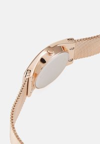 Rose gold metal watch with a mesh strap, rounded case, and a smooth, plain back. Features a single crown on the side for adjustment.