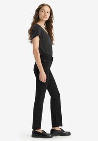Jeans negros ajustados con pierna recta, cintura alta y bolsillos frontales, combinados con una camiseta negra de manga corta y mocasines negros.
