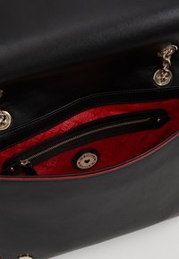 Černá kožená kabelka s červeným vzorovaným interiérem, zlatými kovovými doplňky a zipovou kapsou. Uvnitř je výrazné brandové označení.