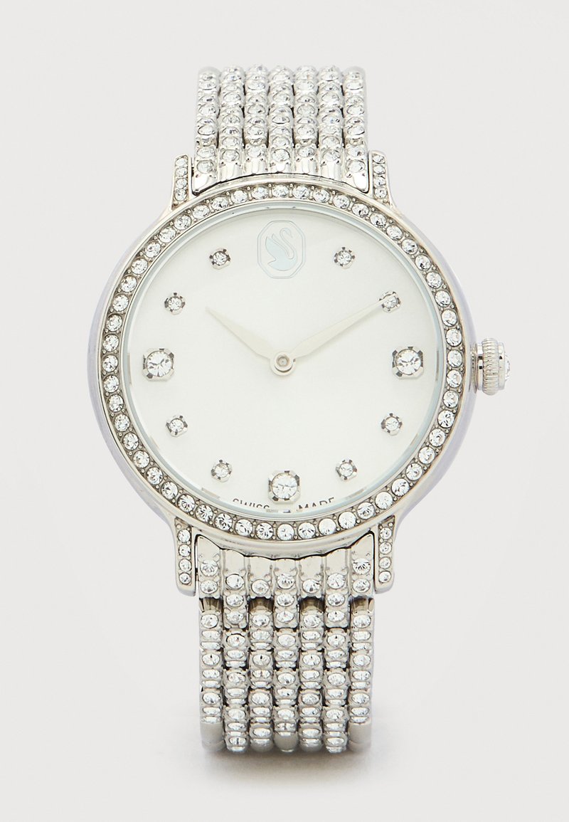 Ασημένιο ρολόι χειρός με στεφάνη, λουράκι και δείκτες ώρας διακοσμημέ νους με κρύσταλλα, λευκό καντράν και απλά ασημένια δείκτες ώρας και λεπτών.