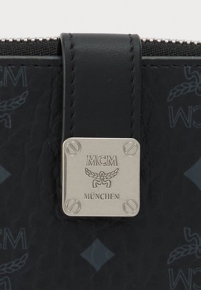 Accessoire en cuir noir avec une plaque logo carrée argentée MCM München et un fond à motif présentant le texte MCM et des motifs de laurier.