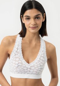 Weißes Spitzen-Bralette mit tiefem V-Ausschnitt und gewellten Kanten. Verfügt über ein weiches Band unter der Brust zur Unterstützung. Texturiertes Blumenmuster über das gesamte Oberteil.