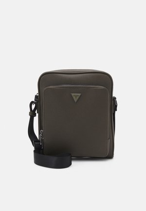 Compact olijfgroene crossbodytas met voorvak met ritssluiting, zwarte verstelbare band en driehoekig metalen merklogo op het voorvak.