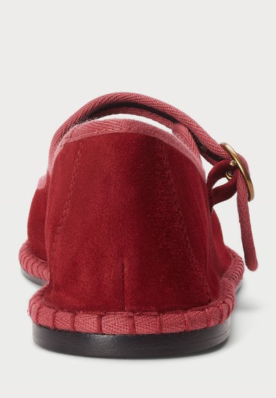 Dos de chausson en daim rouge avec un liseré tissé et une sangle en tissu ornée d'un accent en métal doré. Texture douce et forme arrondie.