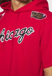 Sudadera roja con "Chicago" en letras blancas y negras. Presenta un parche de baloncesto y el logo de las Finales de la NBA de 1996. Tejido suave, diseño de tipo pullover.