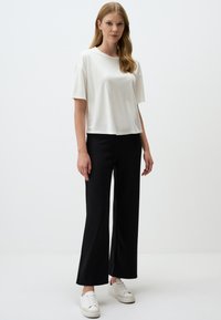 T-shirt bianco a maniche corte con vestibilità morbida, abbinato a pantaloni neri a gamba larga e sneakers bianche. Tessuto morbido, design minimal.