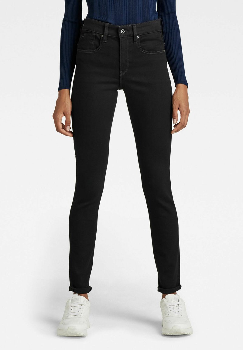 Svarta skinny jeans i denim med en mjuk textur, med hög midja, fem fickor och uppvuxna ärmar, kombinerat med vita sneakers.