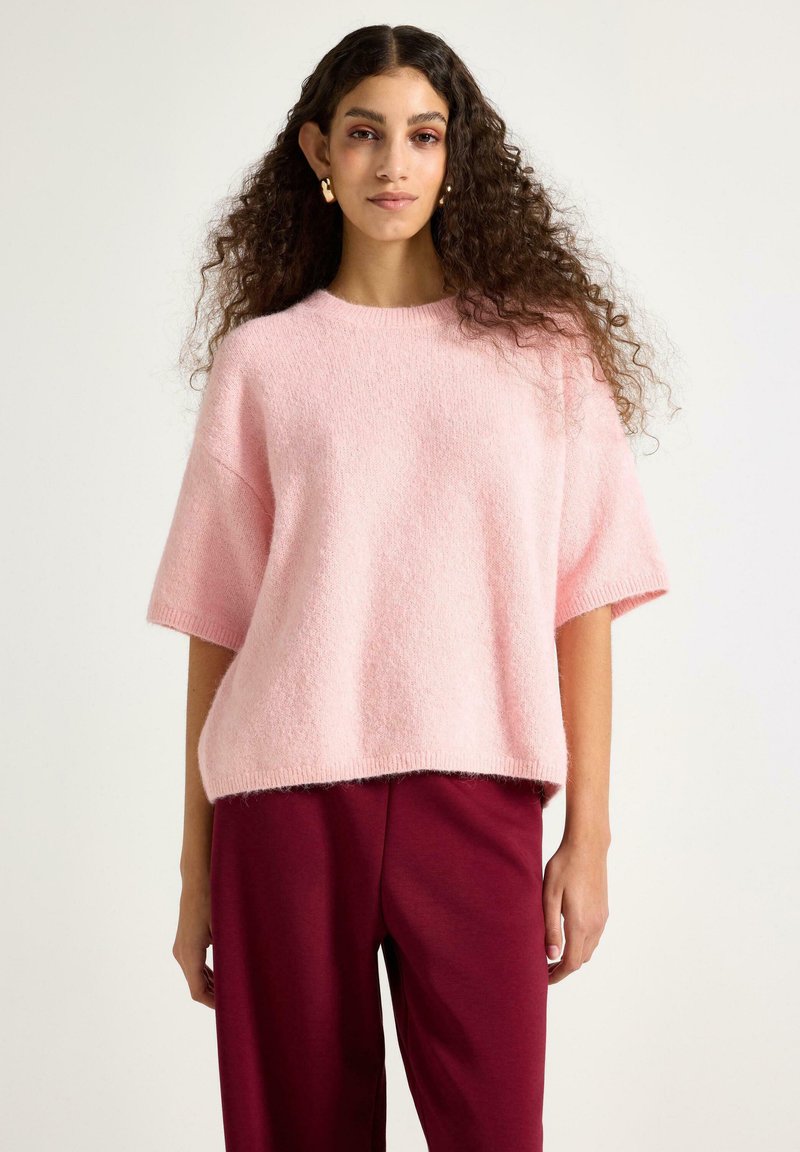 Lyserød strikket kortærmet sweater med en afslappet pasform, der har en blød tekstur og rund halsudskæring, kombineret med mørkerøde bukser.