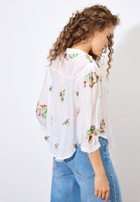 Lightweight white blouse with colorful floral embroidery, billowy sleeves, and a loose fit. Paired with high-waisted blue denim jeans.