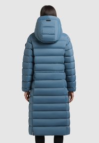 Padded long coat w kolorze jasnoniebieskim, z poziomym przeszyciem, dużym kapturem i boczną metką z logo. Gładki, wodoodporny materiał.