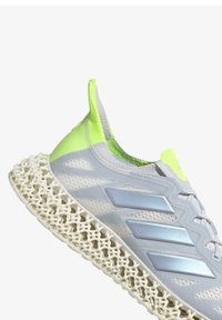 Scarpa atletica grigia con tomaia in rete testurizzata e accenti verde neon. Presenta una distintiva intersuola bianca a rete e tre strisce metalliche.
