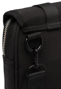 Sac en tissu noir présentant une surface texturée, une fermeture éclair argentée et du matériel noir avec un attache-clip et un détail de sangle tissée.