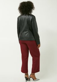 Giacca di pelle nera con cuciture curve, abbinata a pantaloni larghi bordeaux. La modella indossa tacchi neri con cinturini trasparenti.