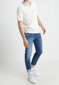 Vit texturerad polo skjorta med ljusblå krage, i kombination med blekta blå denimjeans och vita sneakers med uppvikta cuffs.