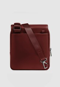 Bolso mensajero de cuero burdeos con correa de hombro ajustable, textura suave, bolsillo lateral con cremallera y detalles de herrajes metálicos.