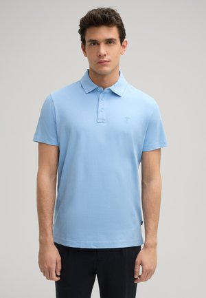 Lichtblauw poloshirt van zachte katoen. Heeft een klassieke kraag, drie knopen en een klein geborduurd logo op de borst.